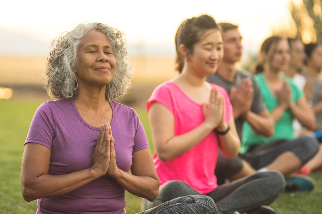 A senior woman of Pacific Islander descent meditates during a group yoga class.