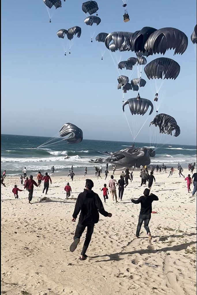 This image grab from an AFPTV video shows Palestinians running toward parachutes attached to food parcels, air-dropped from US aircrafts on a beach in the Gaza Strip on March 2, 2024.