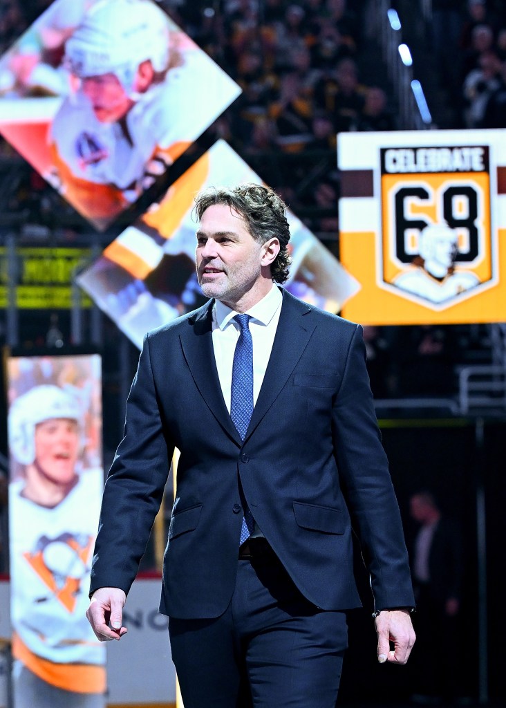 Jaromir Jagr takes the ice for his jersey retirement ceremony, standing in front of a large crowd while wearing a suit.