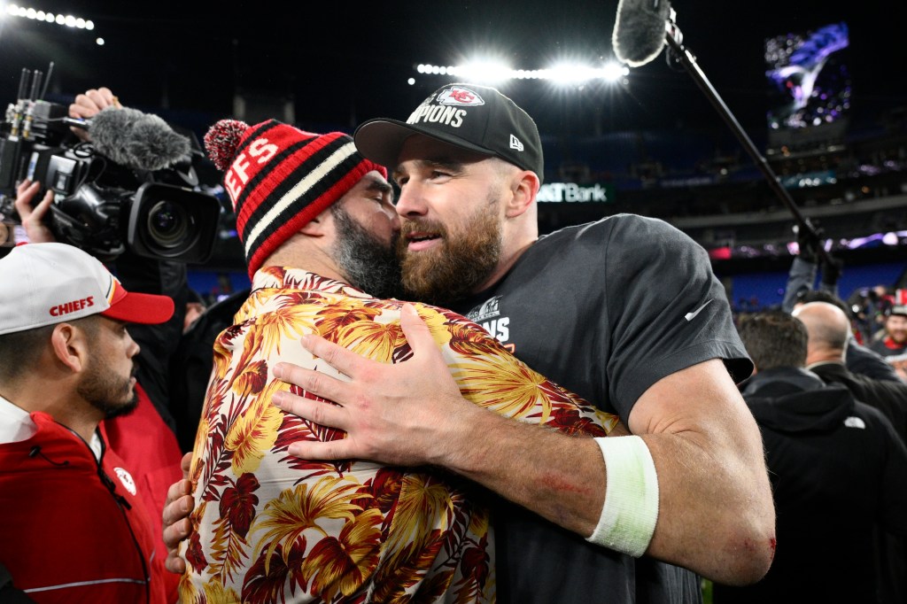 Jason and Travis Kelce hugging after AFC Championship Game while surrounded by people on a football field.