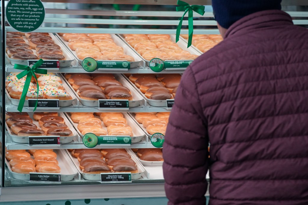 Person observing a variety of doughnuts on display at a Krispy Kreme Doughnuts retail store