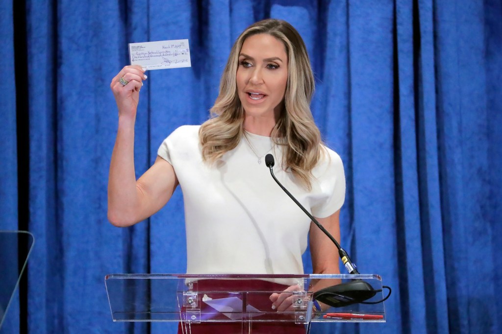 Lara Trump at RNC Spring Meeting, Houston - holding a donation check at a podium with the crowd in the background