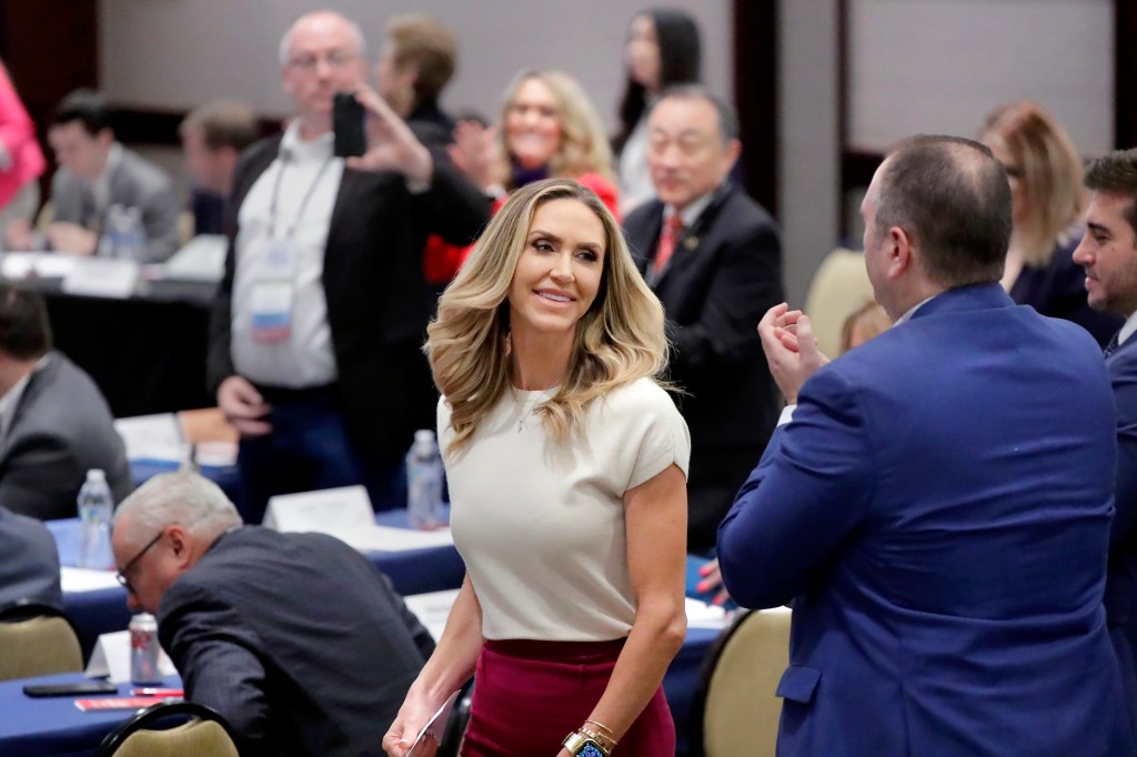Lara Trump in a white shirt and red skirt walks to the podium from the audience during the RNC Spring Meeting 2024.