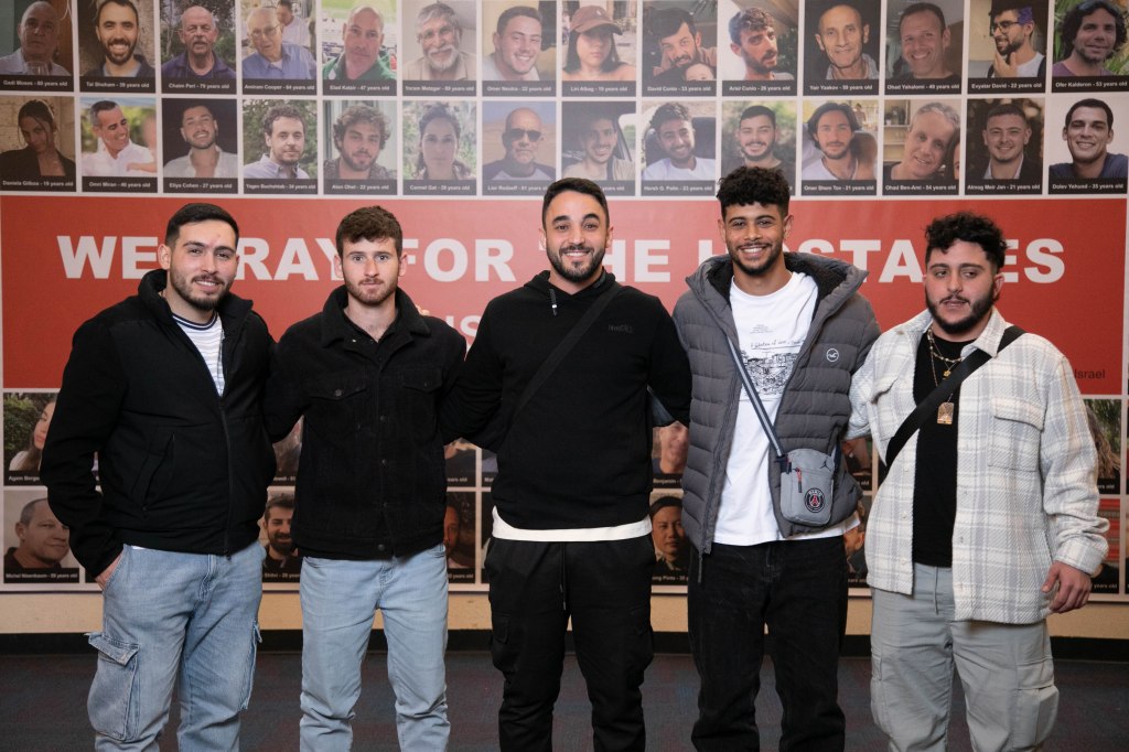 Left to right: Or Kakiashvili, Amichai Beck, Matan Eisenberg, Hillel Ben David, Aviad Mor Yosef standing in front of an array of headshots of the hostages