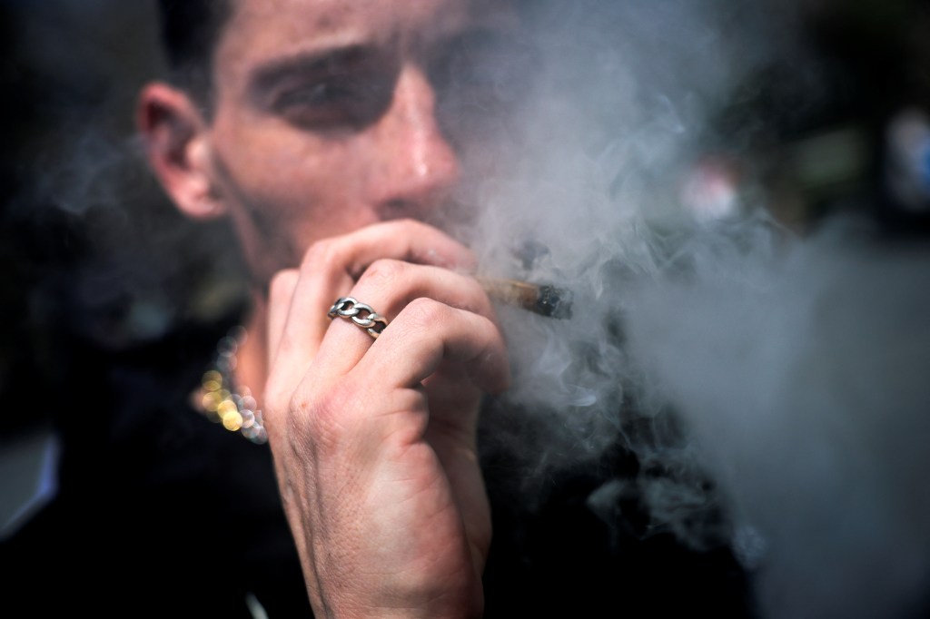 Closeup of a young man smoking a joint, half of his face obscured by a puff of smoke. 