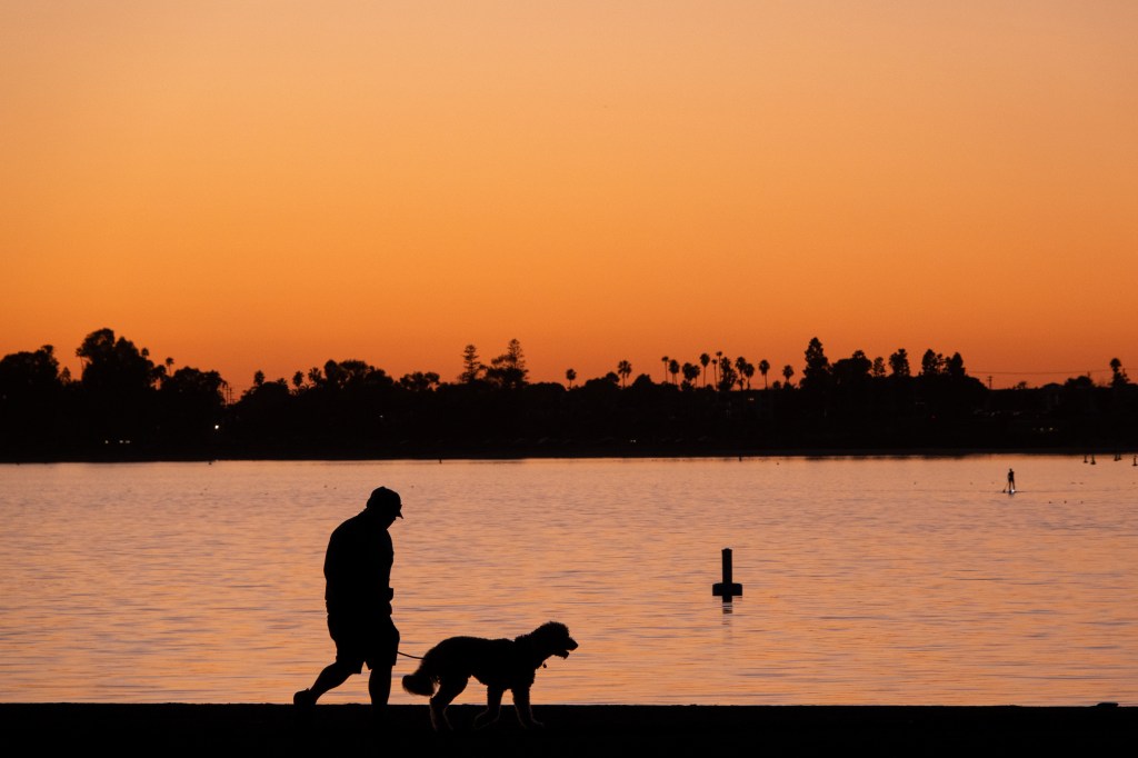 A man walks his dog as the sun sets over Mission Bay Park in San Diego, California.