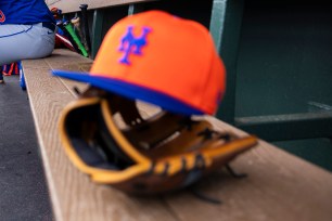 A red and blue New York Mets baseball cap on a bench with a glove, against a stadium background. Luis Severino sits in the distant dugout.