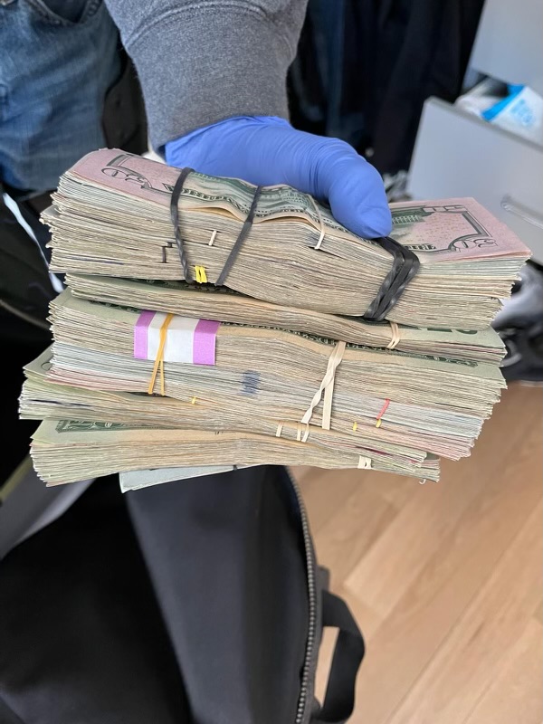 A latex gloved hand holds several large stacks of bills held together with rubber bands.