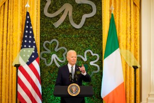 A man, Joe Biden, standing at a podium with flags behind him.