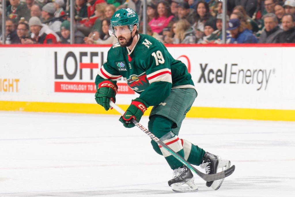 A hockey player in green and white uniform holding a hockey stick, Nic Petan #19 of Minnesota Wild.