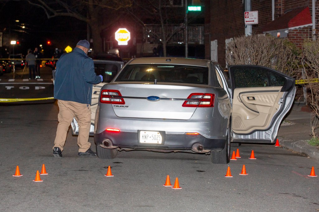 A NYPD officer investigates the scene of officer-involved shooting in Brooklyn, where a car with its four doors open is behind crime scene tape. 