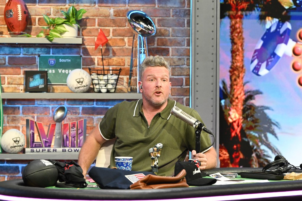 Pat McAfee hosting his show on Radio Row at Mandalay Bay Convention Center, Las Vegas with a microphone on the desk.