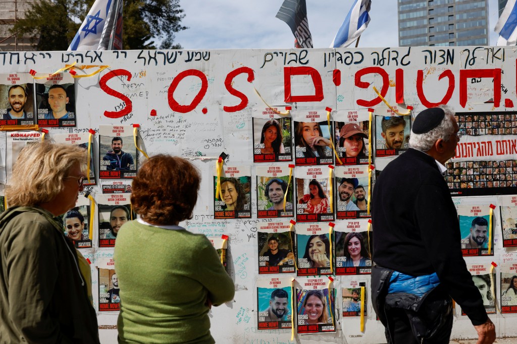 Two women and a man look at posters with photos of hostages kidnapped in the deadly October 7 attack on Israel.