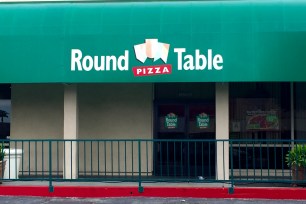 Round Table Pizza restaurant sign on a building with a green awning in Lakewood, California.