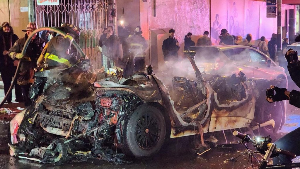 A burned Waymo car surrounded by firefighters in San Francisco.