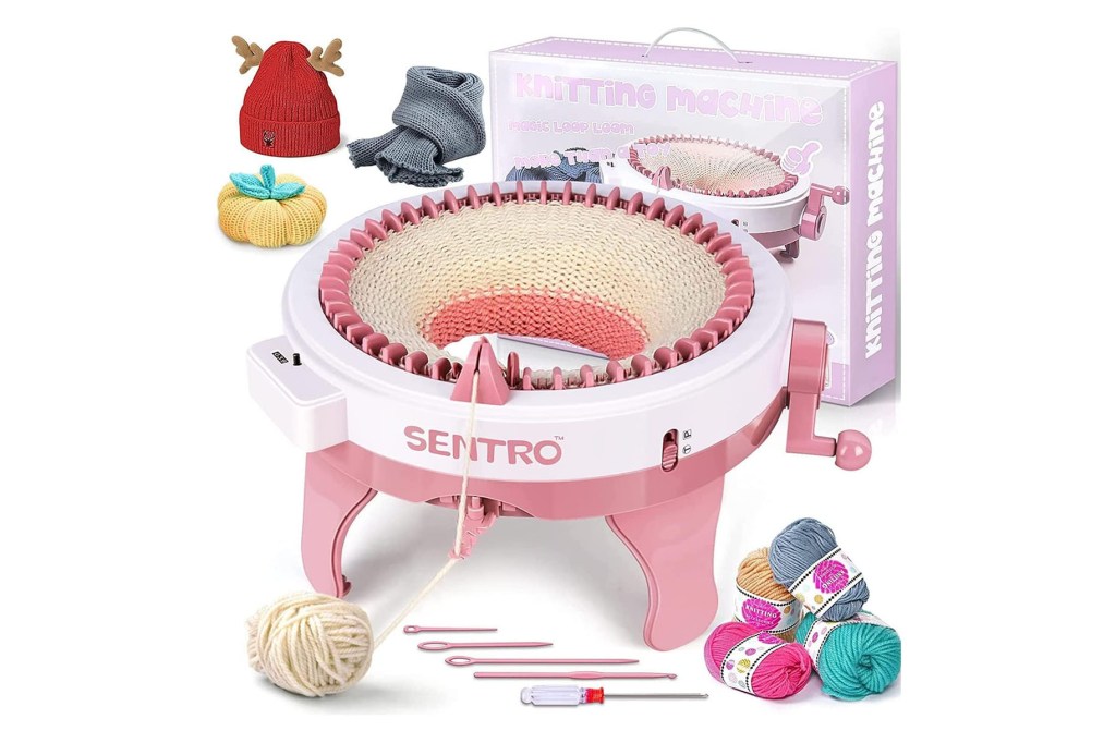 A pink and white knitting machine with a box of yarn and needles