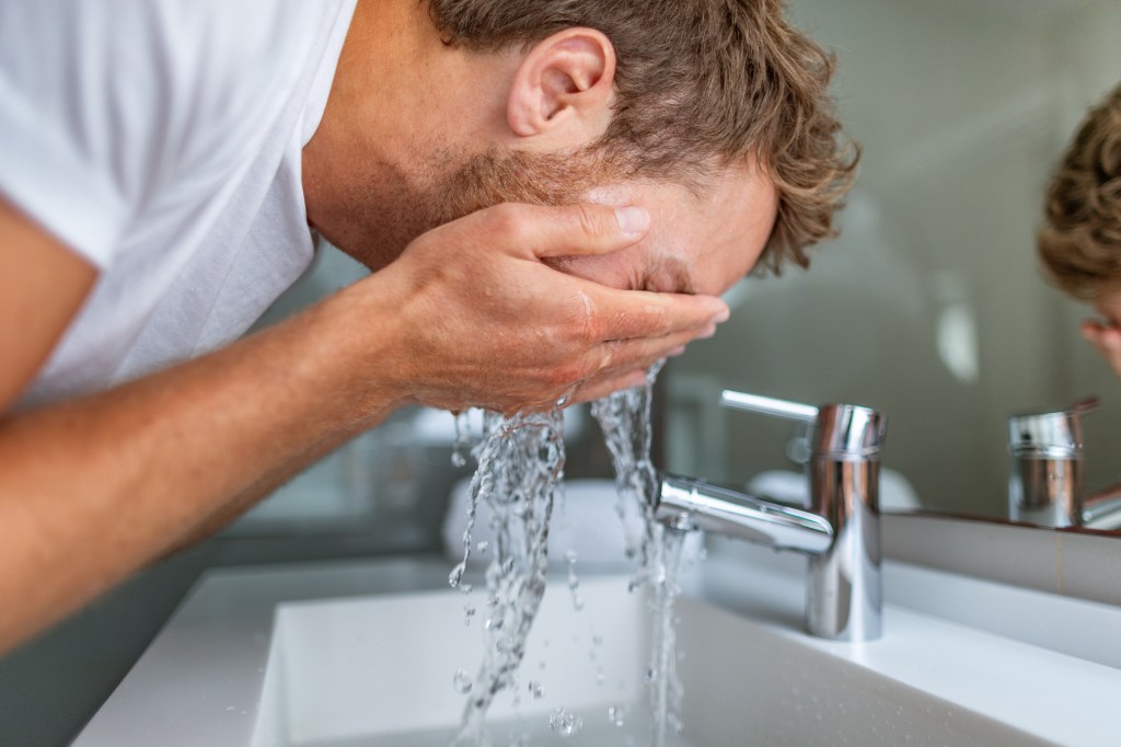 Man cleansing face with cold water in bathroom sink for acne treatment