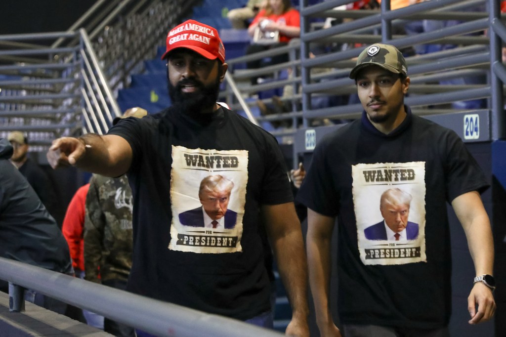 Two men wearing shirts depicting Donald Trump's mugshot as a Wanted poster