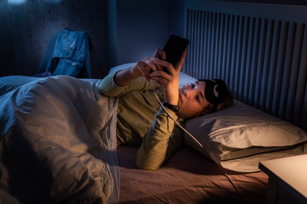 Teenage girl lying in bed at night, using her smartphone due to sleeping disorders