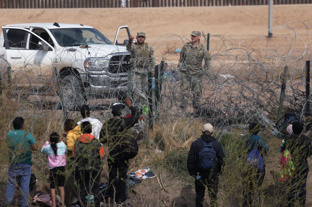 Texas National Guard agents blocking barbed wire fence, preventing Venezuelan migrants from crossing, at El Paso Sector Border.