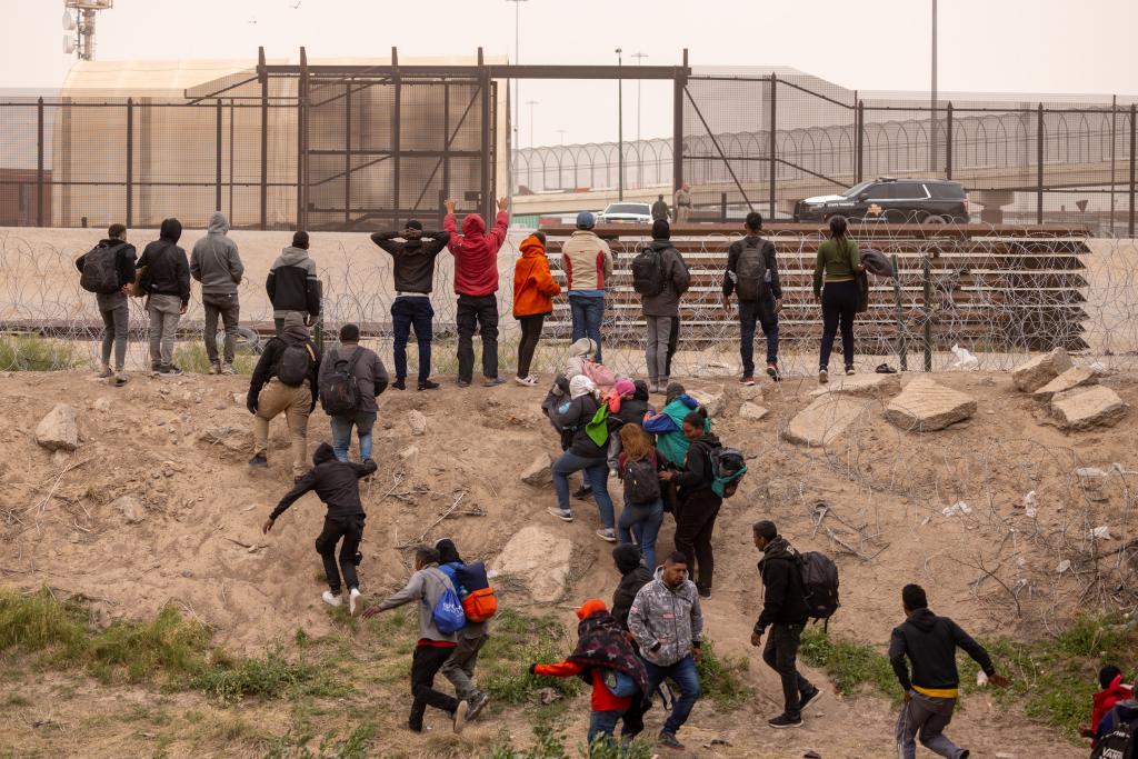 Migrants attempt to enter the US through a cap in the wire fencing installed in Texas.