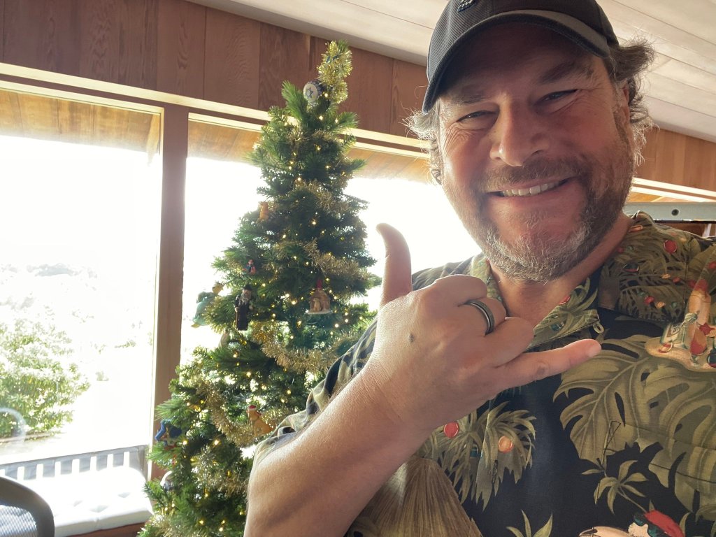 Marc Benioff in a Hawaiian shirt, wearing a hat and making a hand gesture.