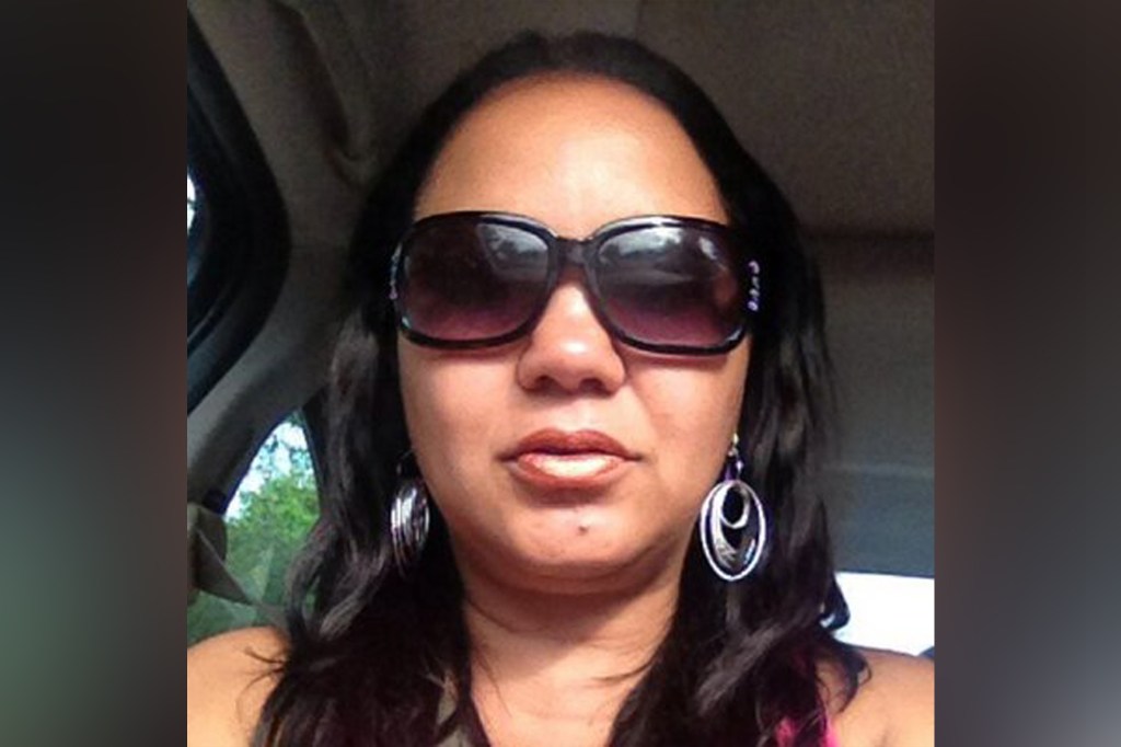Maritza Ming, in sunglasses and wiith silver hoop earrings, sitting in a car staring at the camera