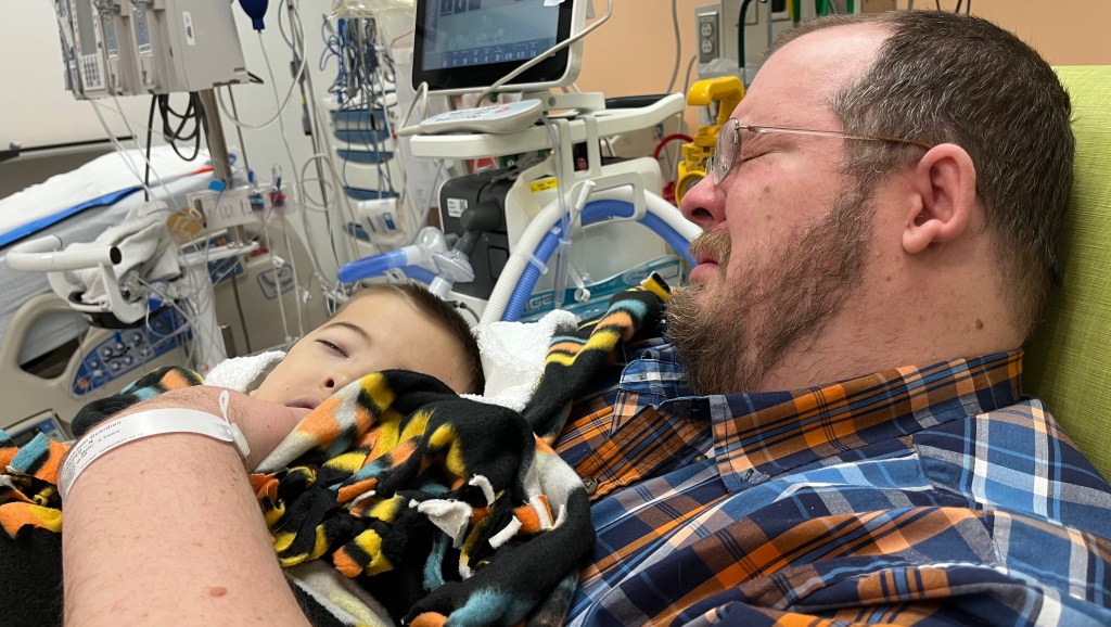 Little Dallin alongside his father as he lay in the hospital after suffering a fatal head injury falling from a slide