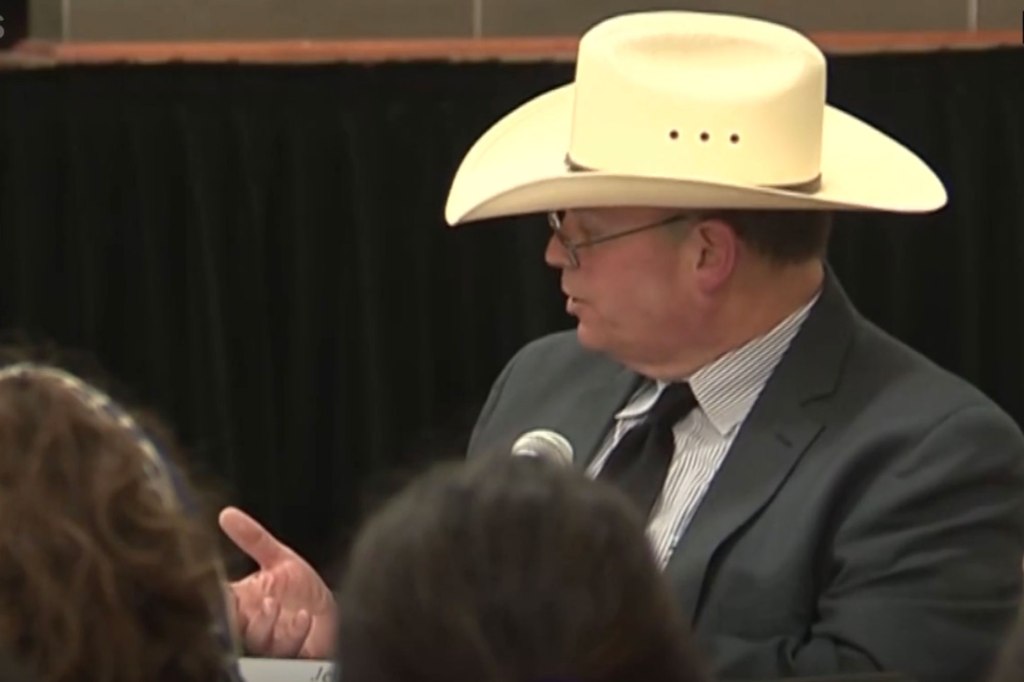 Man in cowboy hat and suit talks into microphone 