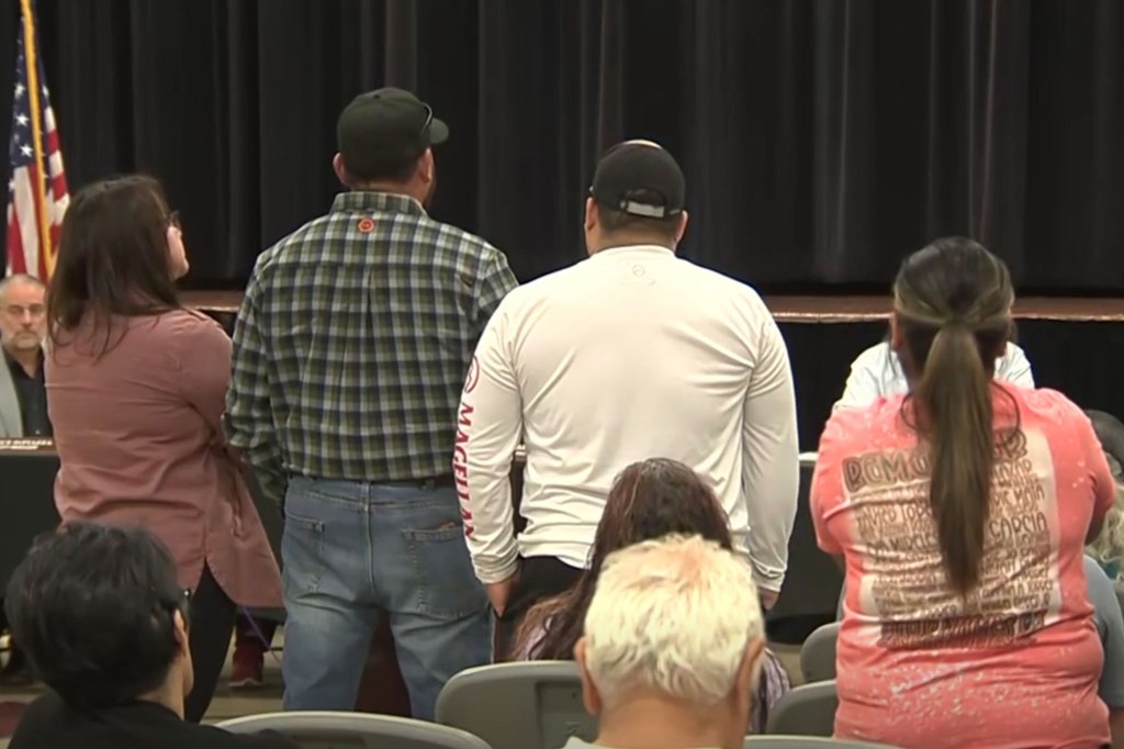 People stand at their seats facing a stage