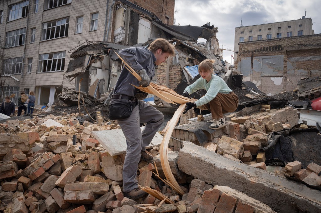 A young man and a woman, both volunteers, clear rubble from Kyiv State Arts Academy after it was hit by a Russian missile.