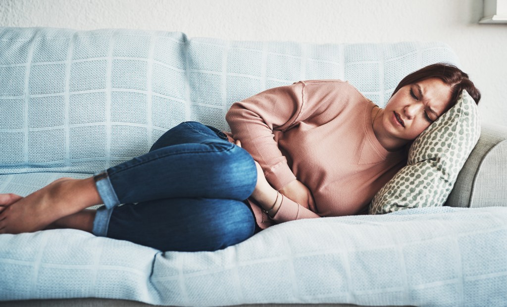 Woman, stomach ache or pain on home sofa 