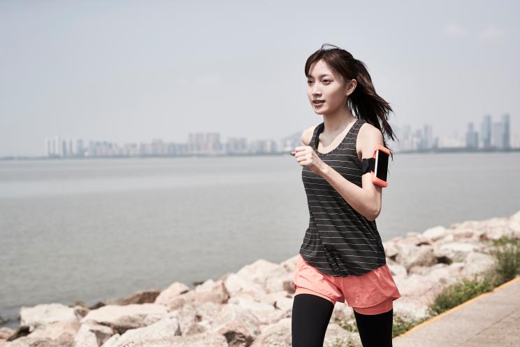 young asian woman jogging by the sea with rocky beach in background