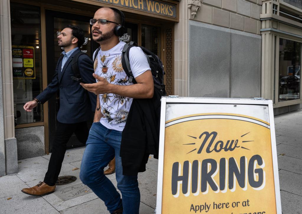 People walking past a restaurant with a hiring sign in Washington, DC, symbolizing significant job growth in the US private sector