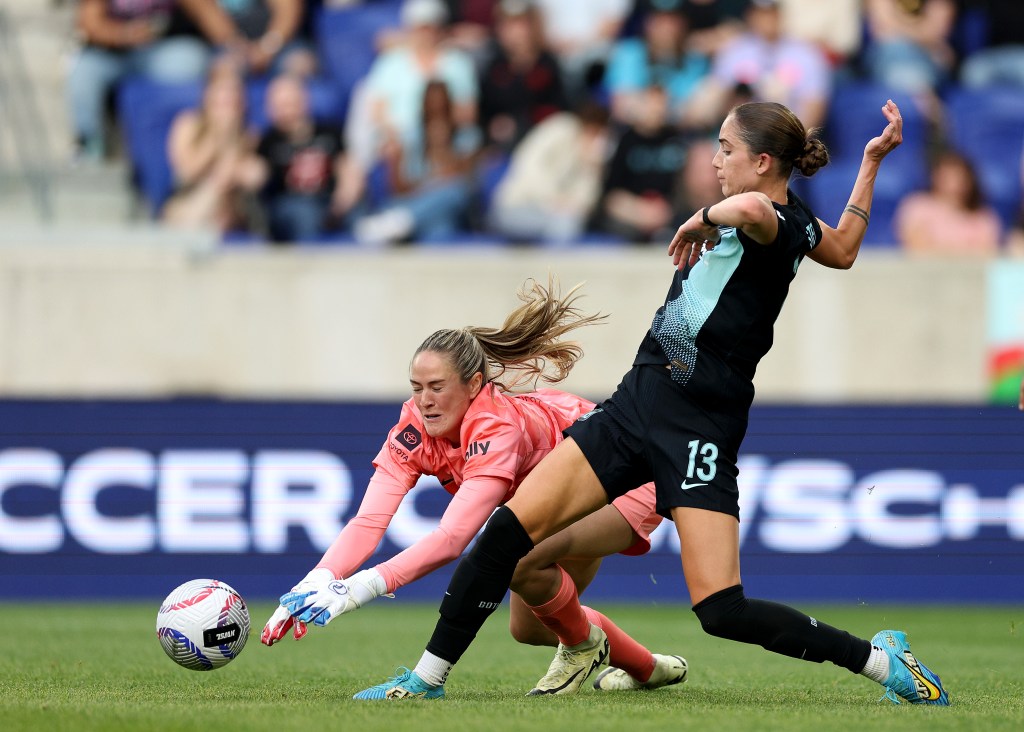 Katie Lund #1 of Racing FC falls as Ella Stevens #13 passes and gets the assist on a goal scored by teammate Rose Lavelle during the second half on Sunday.