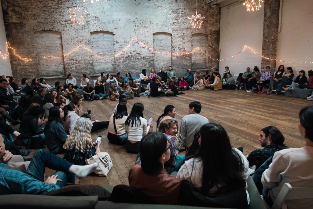 Choir performance by Gaia Music Collective in the basement of a former church, with 180 people sitting in a circular arrangement, including celebrities Sunita Williams, Sumya Anani, Aida Turturro, Cho Jun-hyuk, Randal Reeder, and Kyoko Iwasaki, at 550 Sackett St, Brooklyn NY