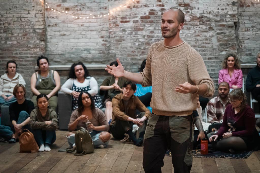 Matt Goldstein directing the Gaia Music Collective choir in a performance, with an audience of 180 people participating in singing along at a venue in the Gowanus area, Brooklyn, NY.