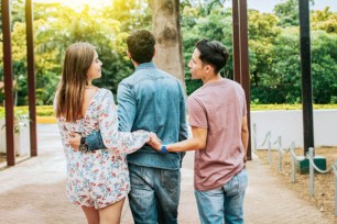 Unfaithful girl walking in the park with her boyfriend while holding another mans hand