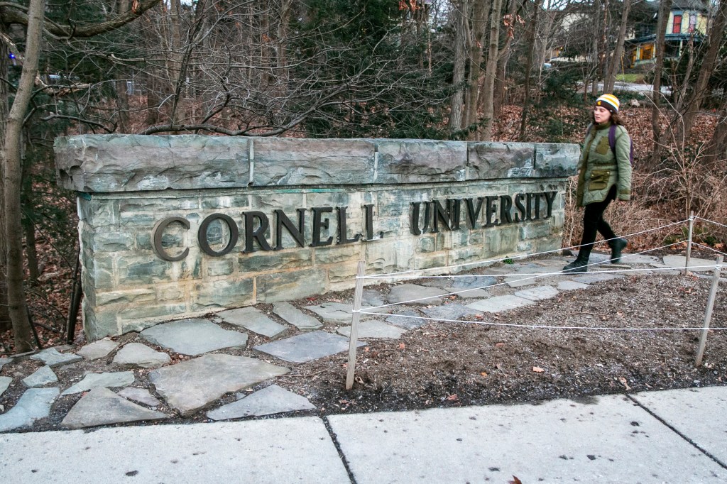 A woman walks by a Cornell University sign
