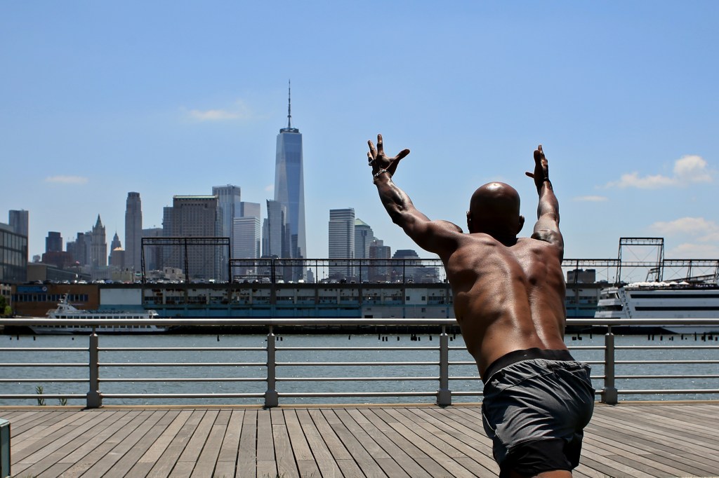 Shirtless man doing stretches as he faces the NYC skyline.