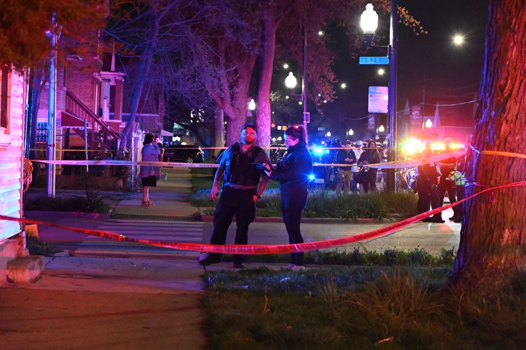 Two police officers standing next to a red tape at the scene of a mass shooting in Chicago, Illinois on April 13, 2024