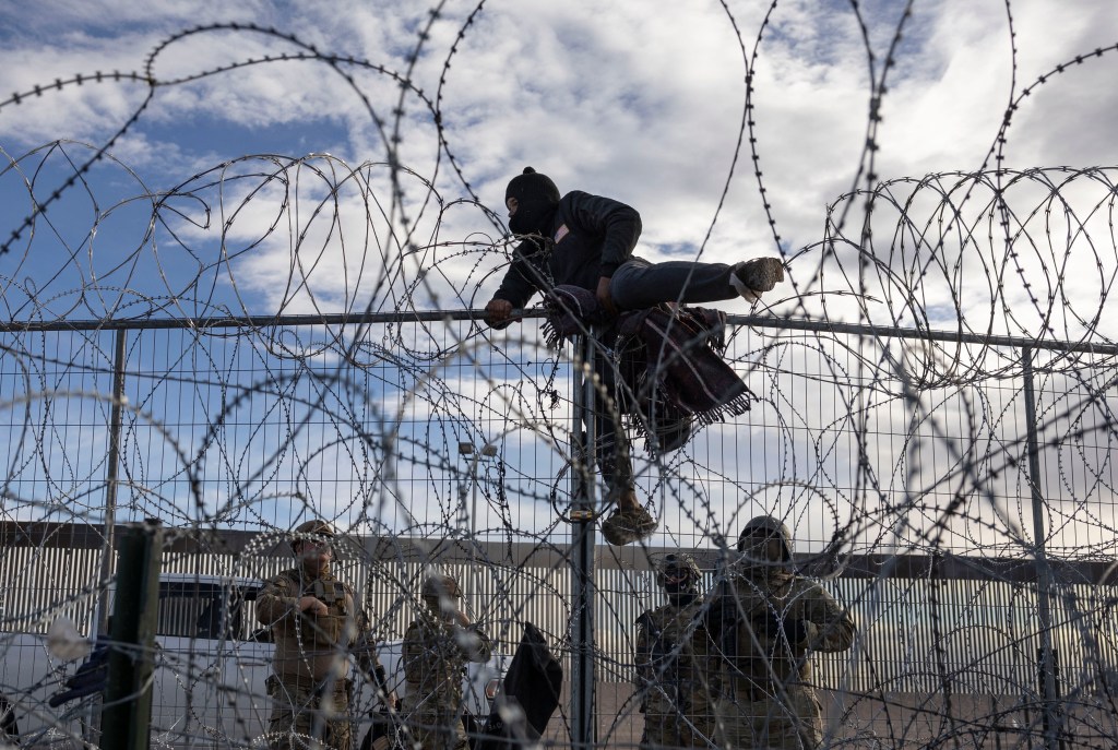 A Venezuelan migrant climbing over a fence near the border in El Paso, Texas on April 2, 2024.