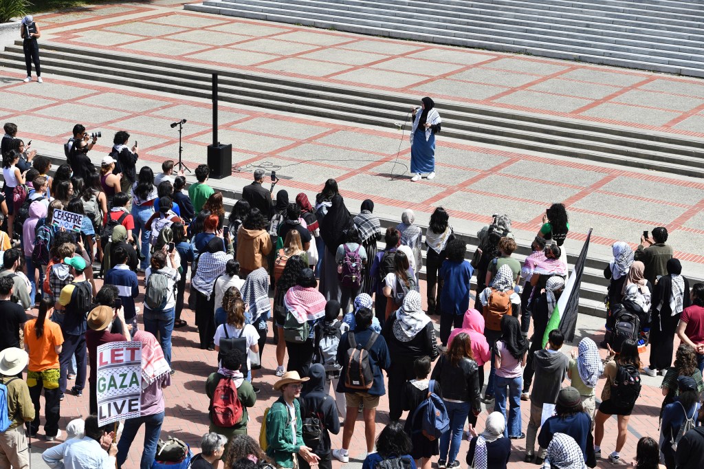 A crowd watching a woman in black hijab and keffiyeh speaking into a microphone