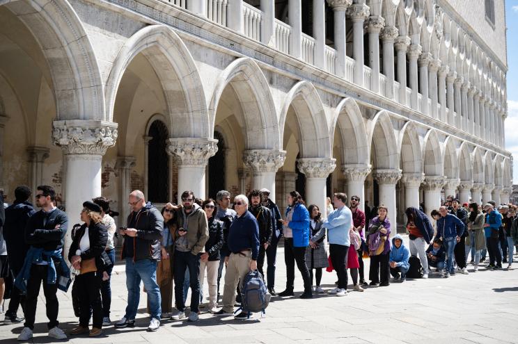 Visitors queueing to enter the Basilica in San Marco Square, Venice, implementing a new fee strategy to reduce tourist numbers, with unknown celebrities in the crowd.