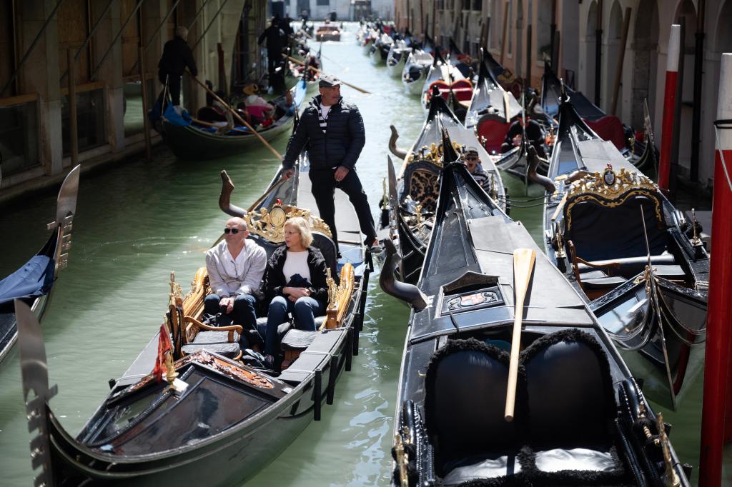 A gondolier sailing with two tourists near San Marco Square in Venice, reflecting the city's strategy to regulate tourism by implementing an entry fee to the historic centre.