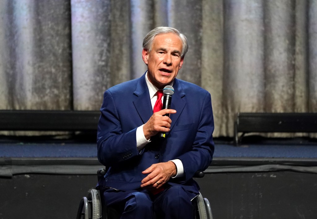 Texas Governor Greg Abbott in a suit and tie, holding a microphone, speaking at the 2024 New York GOP Gala at the New York Hilton Hotel.