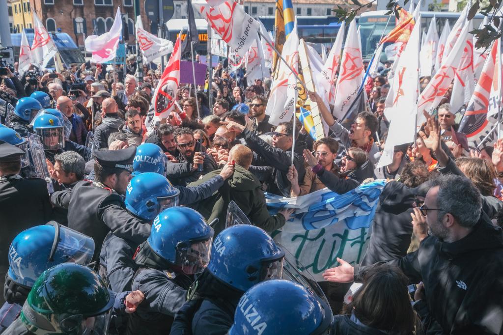 Demonstrators with signs and flags trying to break through police blockade at Piazzale Roma in Venice, Italy, protesting against the new tourist entry fee