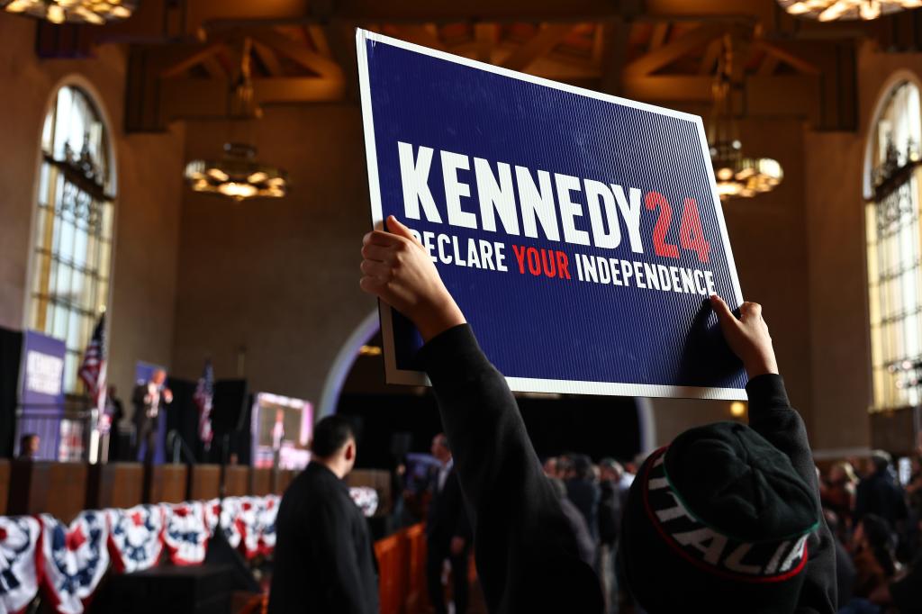 Supporter holding a sign at a Cesar Chavez Day event while Robert F. Kennedy Jr. speaks in the background, campaigning for presidential bid, in Los Angeles, California