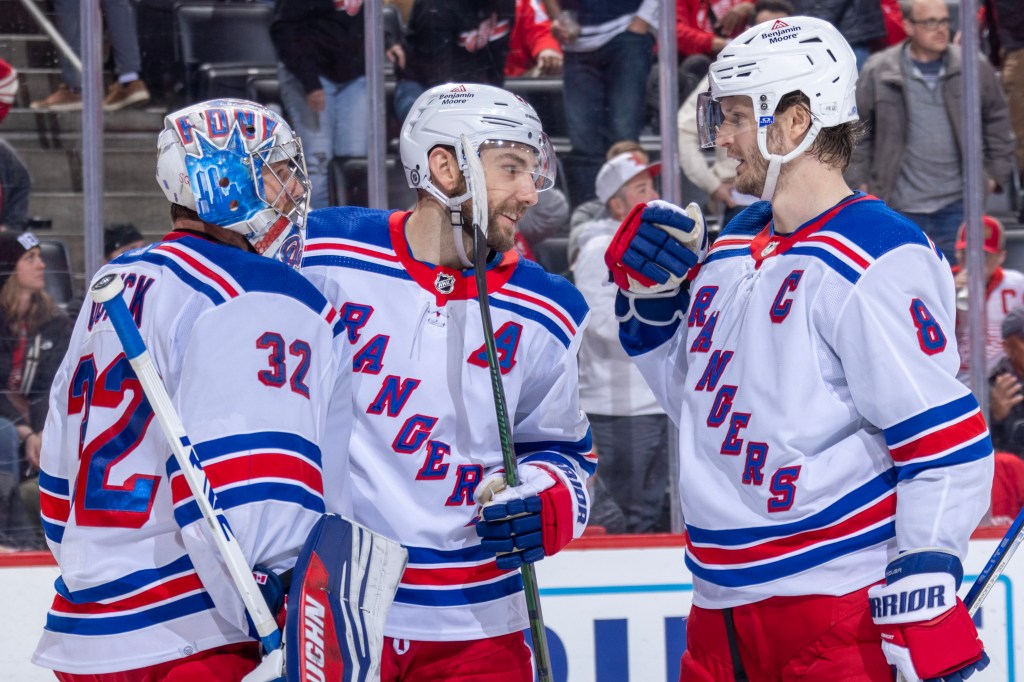 Jonathan Quick #32 of the New York Rangers celebrates the victory over the Detroit Red Wings with Barclay Goodrow #21 and Jacob Trouba #8 at Little Caesars Arena 