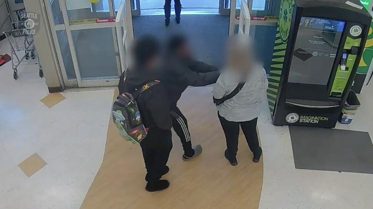 Security camera footage showing two teens approaching a woman at a pharmacy entrance, with one teen snatching her purse from her hands.